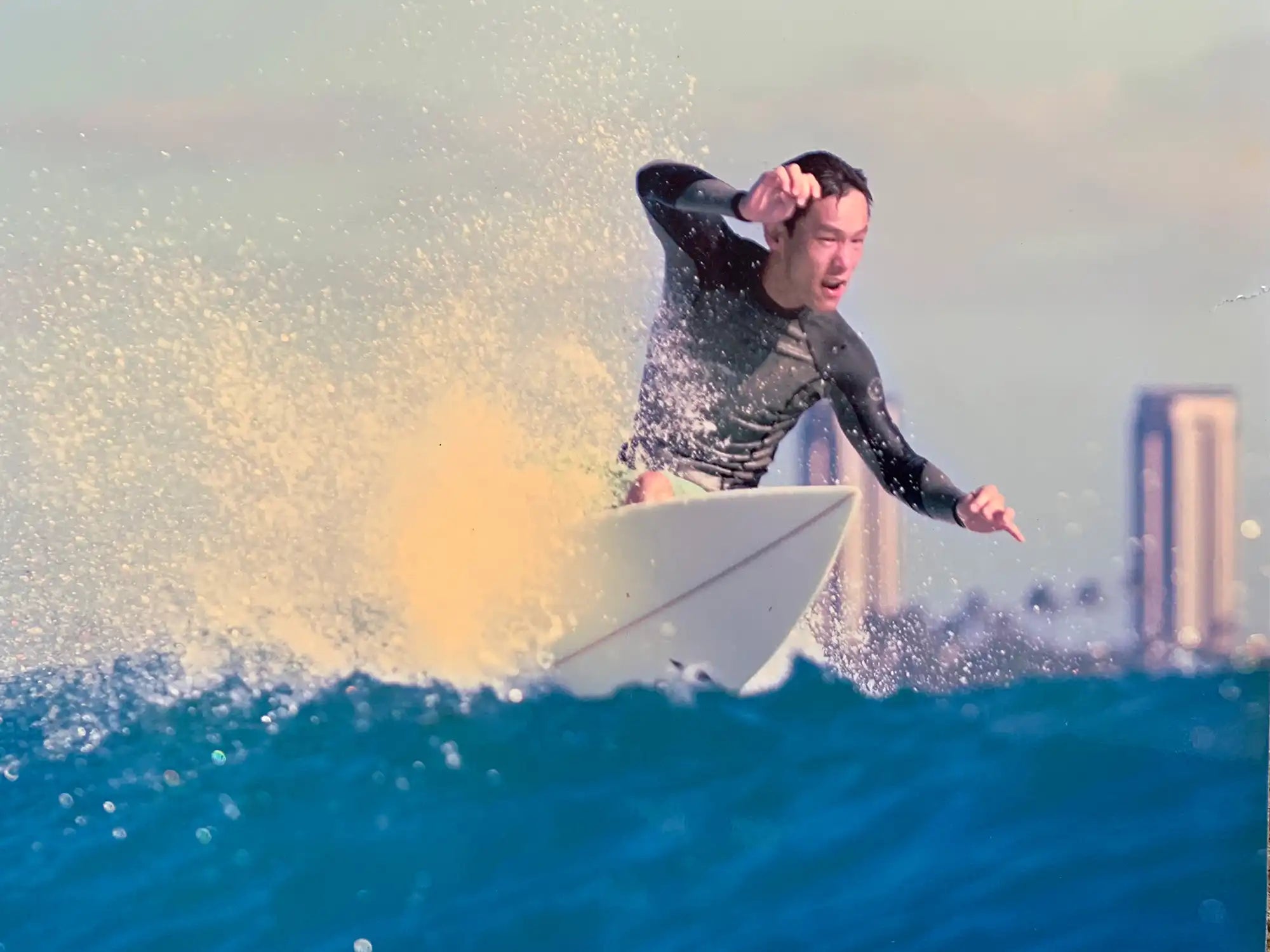 ハワイの海で波に乗り、ダイナミックにターンを決める日本人インストラクターのサーフィンアクション写真。