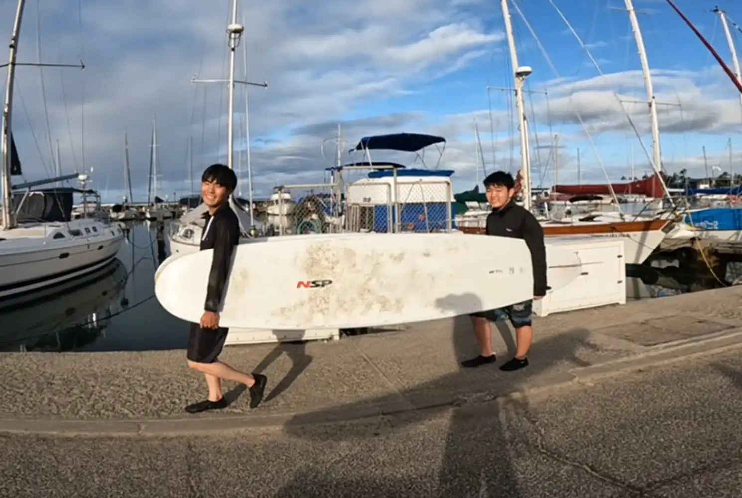 アラモアナのハーバーでレッスンで使うサーフボードを運ぶ二人の生徒。CLIPSハワイのサーフィンレッスン風景。