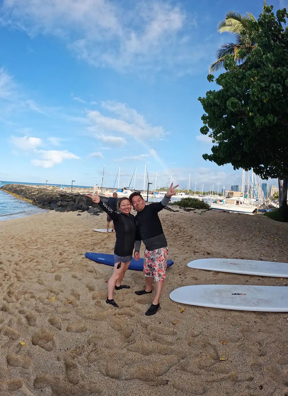 ワイキキ近くのビーチでレッスンを終え、レインボーを背景に楽しそうにポーズをとる参加者のペア写真。