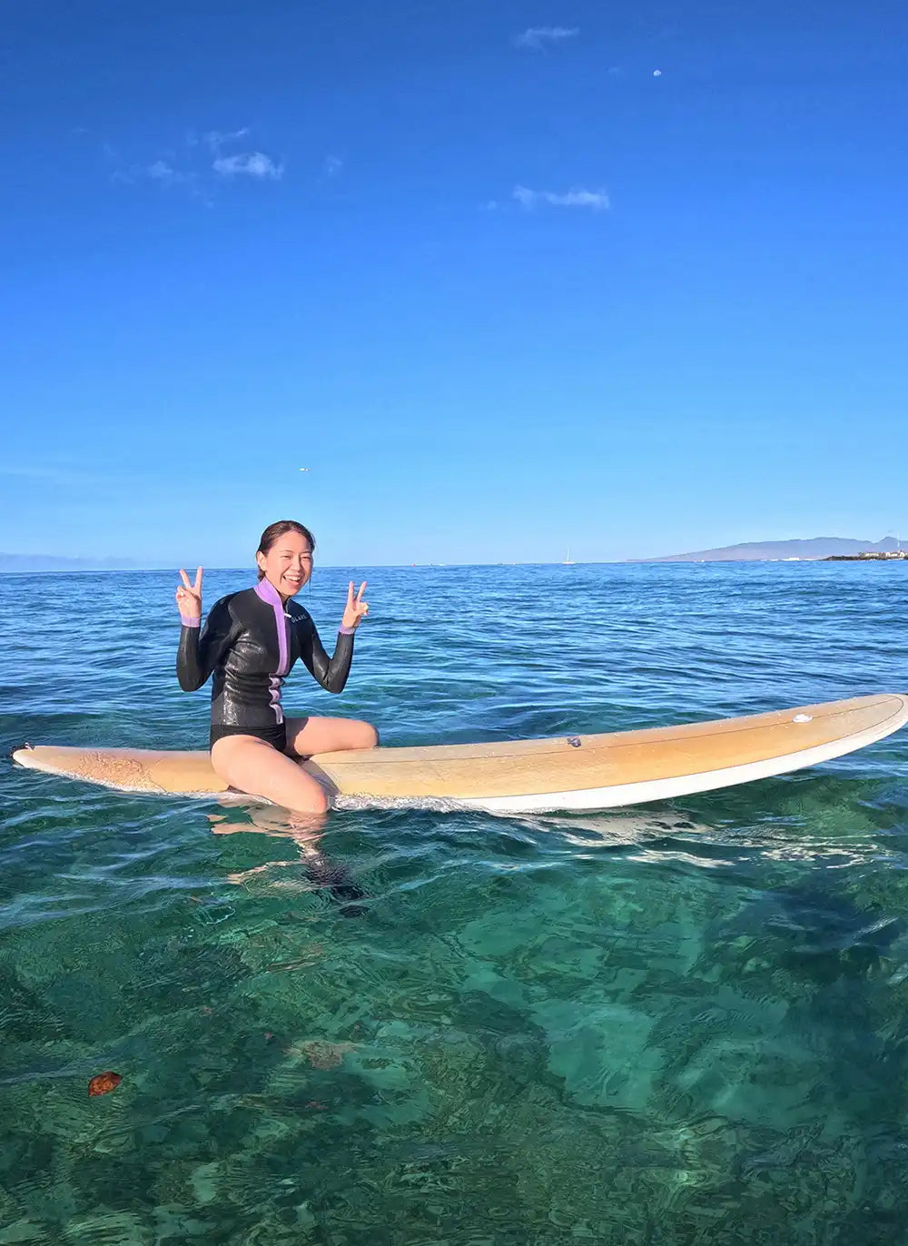 透明度の高い浅瀬でサーフボードに座り、穏やかな海を楽しむレッスン受講者の写真。